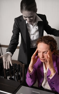 image of a visibly stressed female office worker sat at a desk while a female co-worker shouts at her.